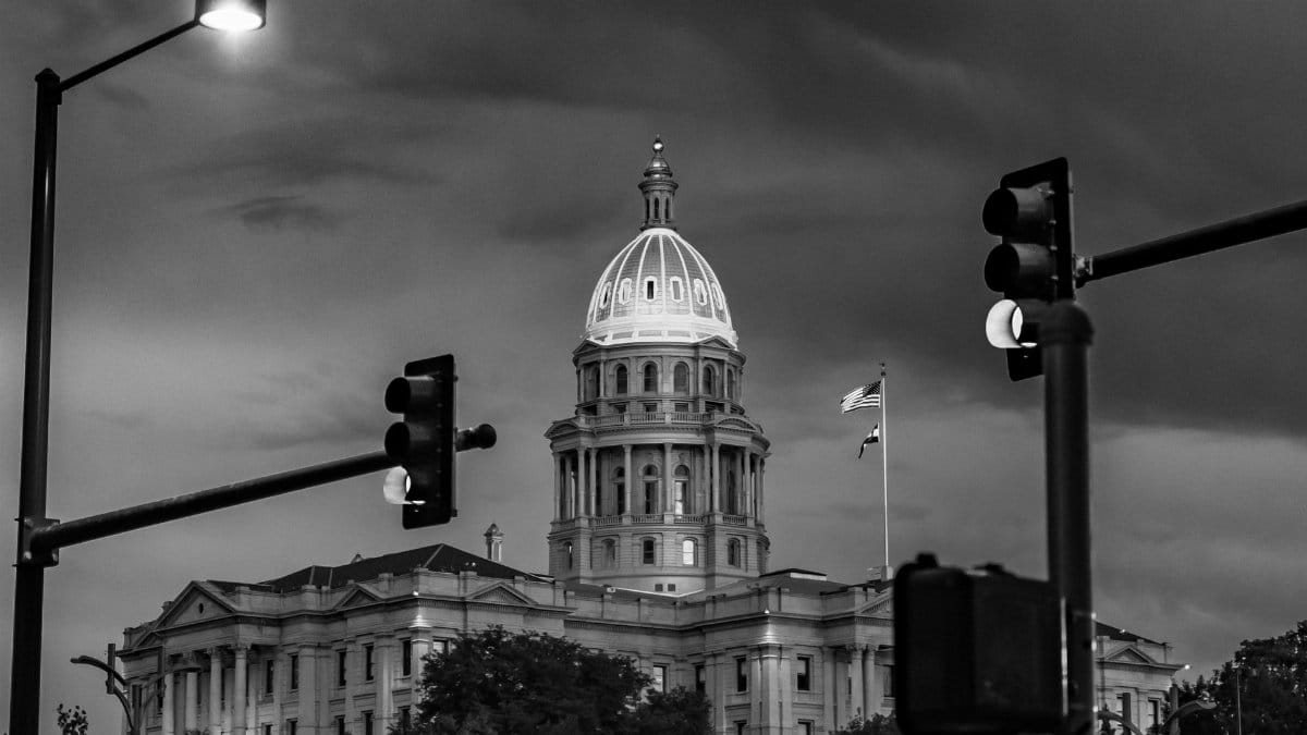 Dramatic black and white photo of the Colorado State Capitol at night with streetlights and stoplights.