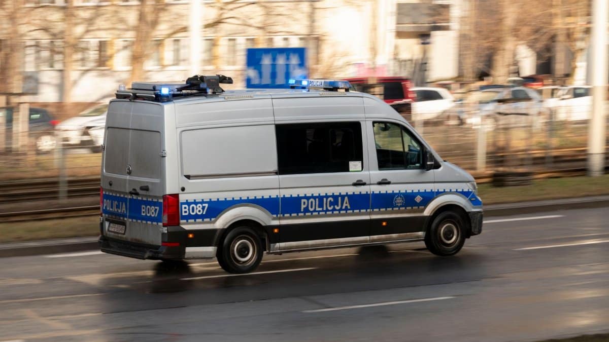 A Polish police van with blue lights on, driving swiftly on a city road.