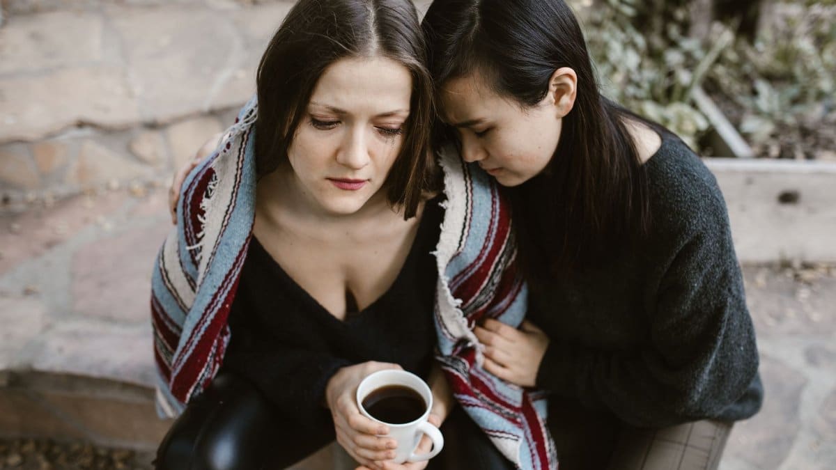 Two women sharing a moment of comfort and warmth with coffee outdoors.