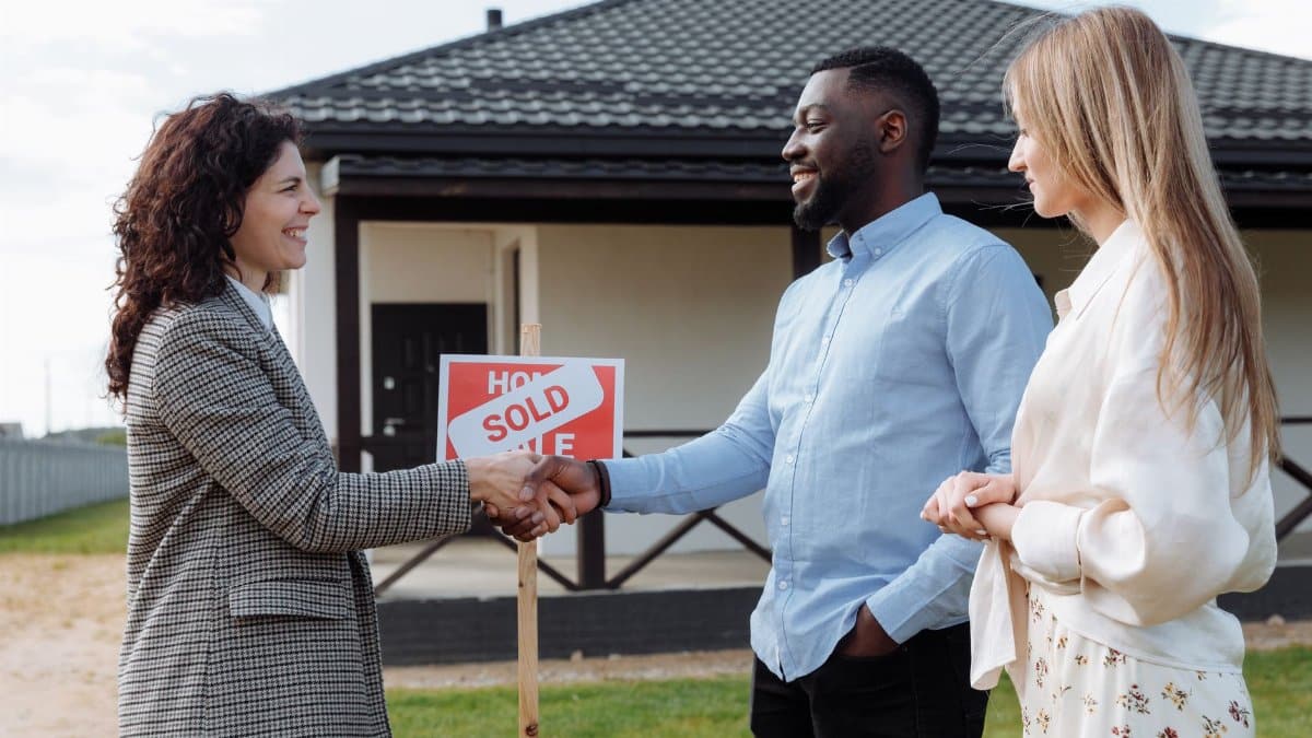 Real estate agent sealing a deal with a diverse couple in front of their new house.