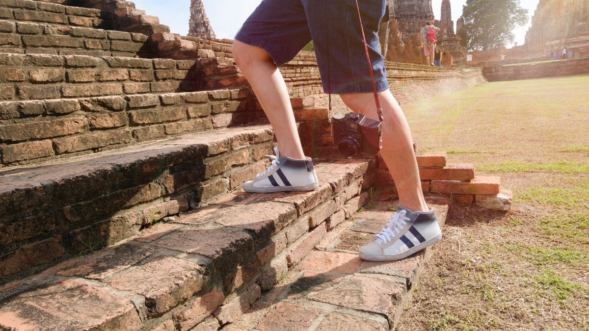 A tourist wearing sneakers climbs ancient brick steps at a historic temple site on a sunny day.