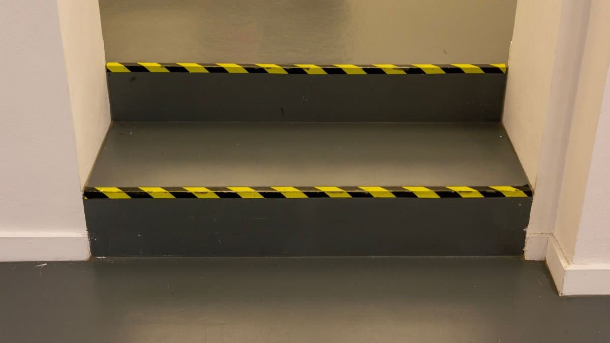 Green steps with black and yellow caution tape in an interior hallway for safety.
