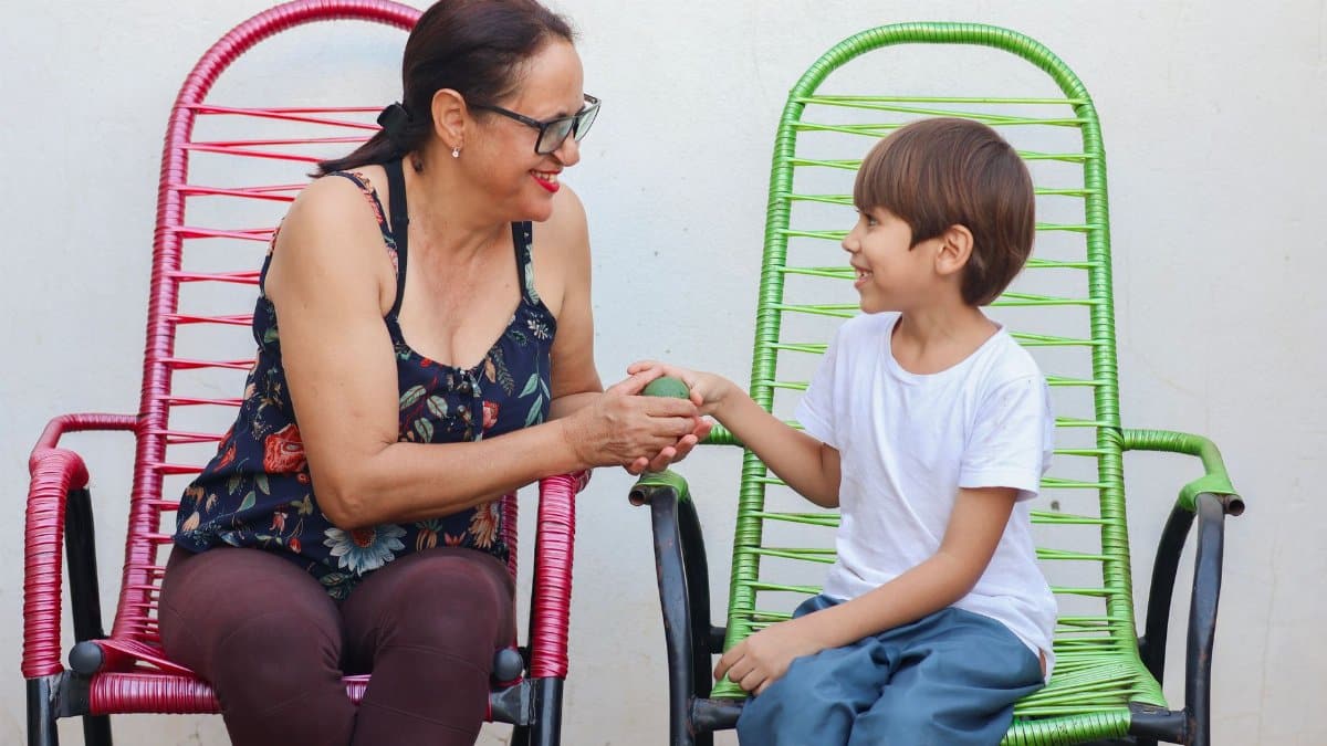 Heartwarming moment between grandmother and grandson sharing a conversation outdoors on vibrant chairs.