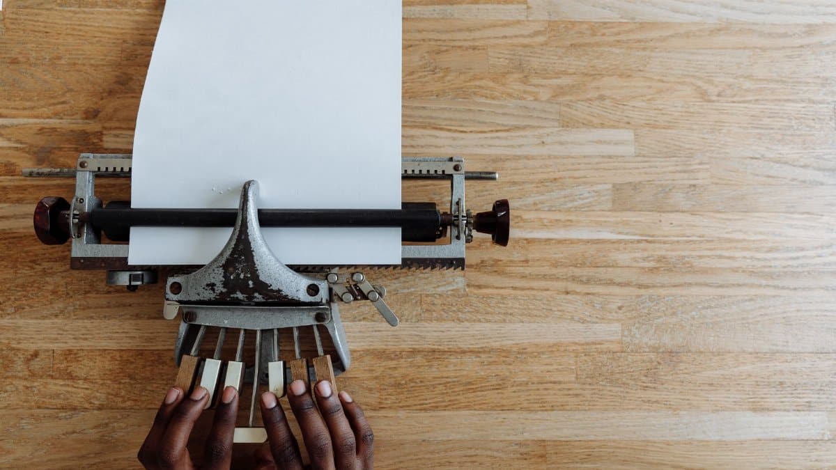 Close-up of hands typing on a braille typewriter for visual impairment on a wooden table.