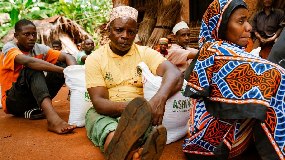 A diverse group sitting outdoors, highlighting vibrant cultural attire in a rural African setting.