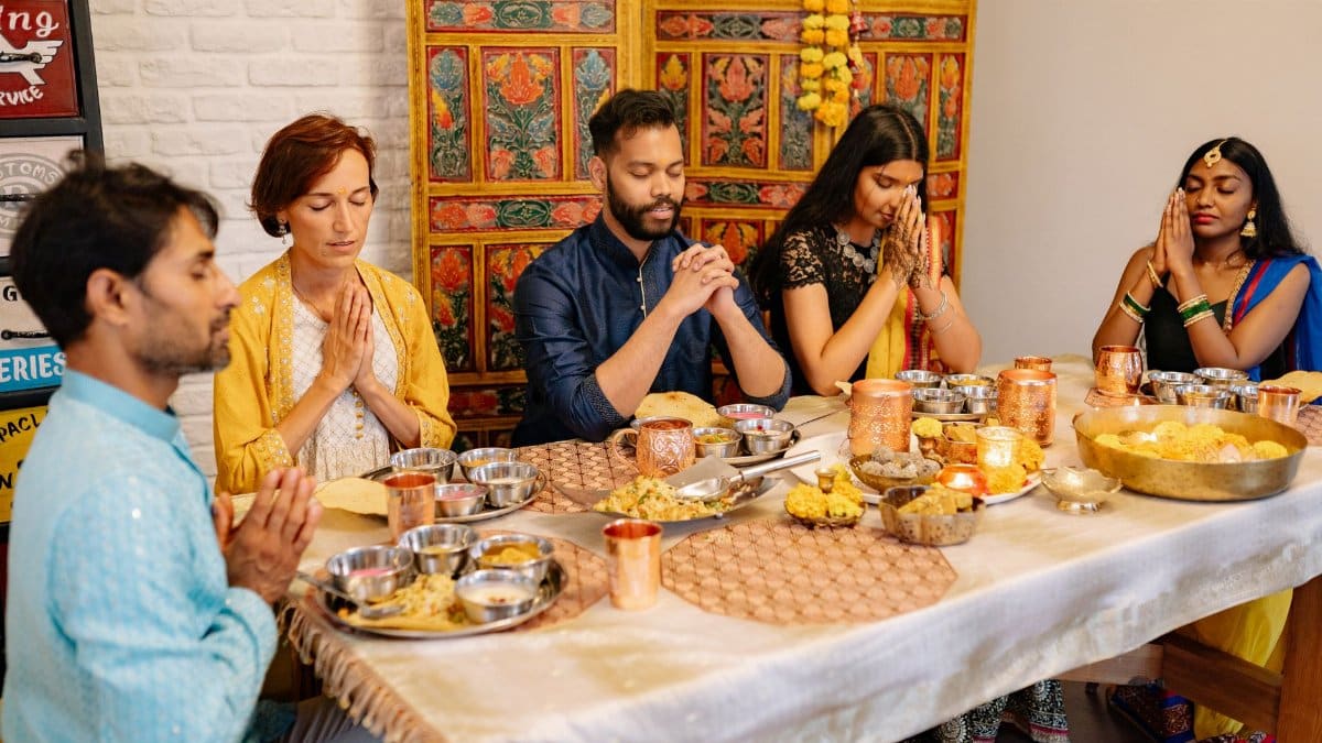 A family around a dinner table praying together during Diwali celebration, indoors.