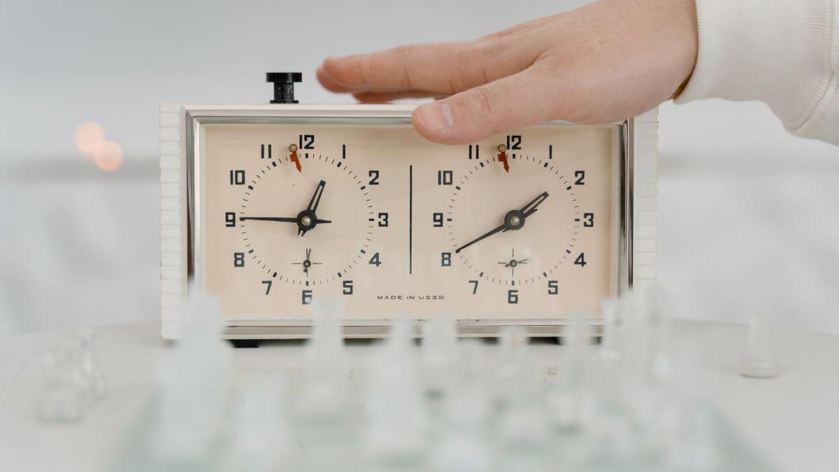 Close-up of a hand adjusting a chess clock during a timed chess game indoors.