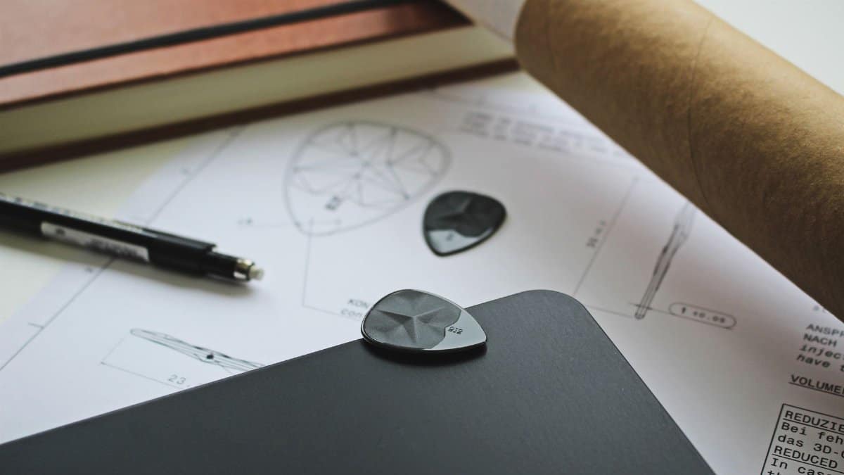 Close-up of guitar pick design on technical drawings and black notebook.