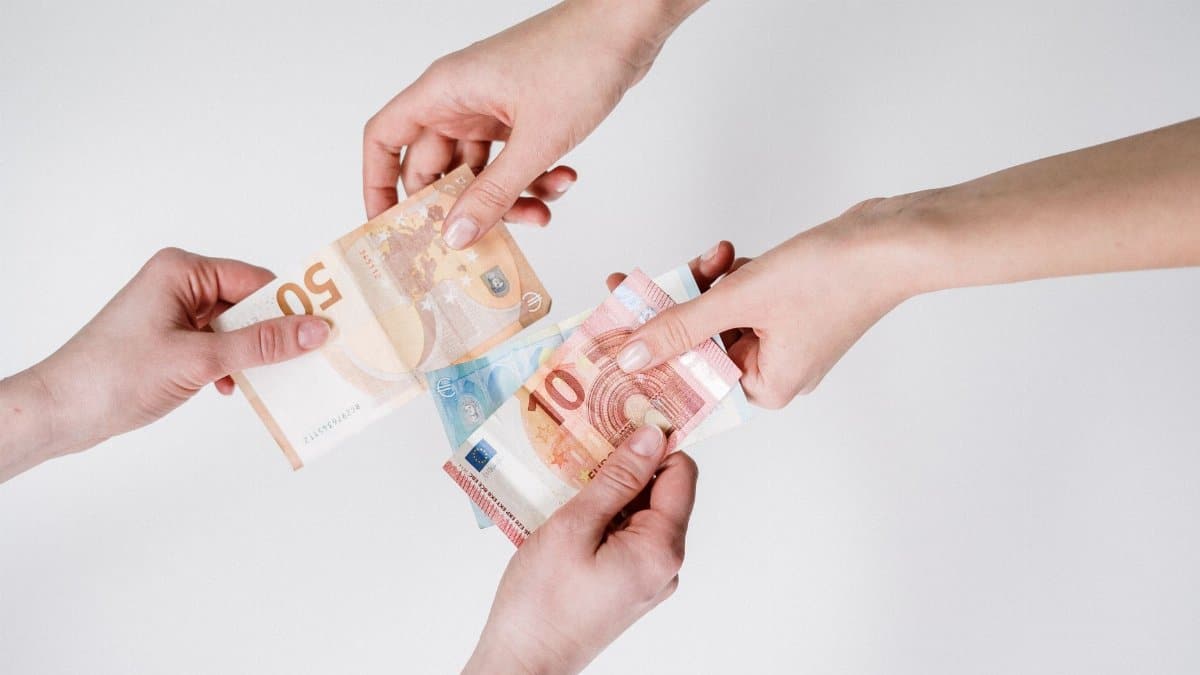 Two pairs of hands exchanging Euro banknotes, symbolizing finance and transaction.