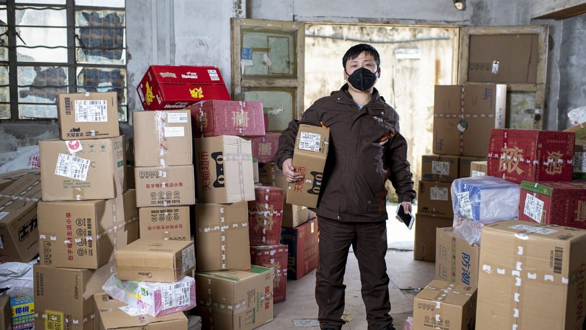 Delivery worker holding packages in a Wuhan warehouse, wearing a face mask.