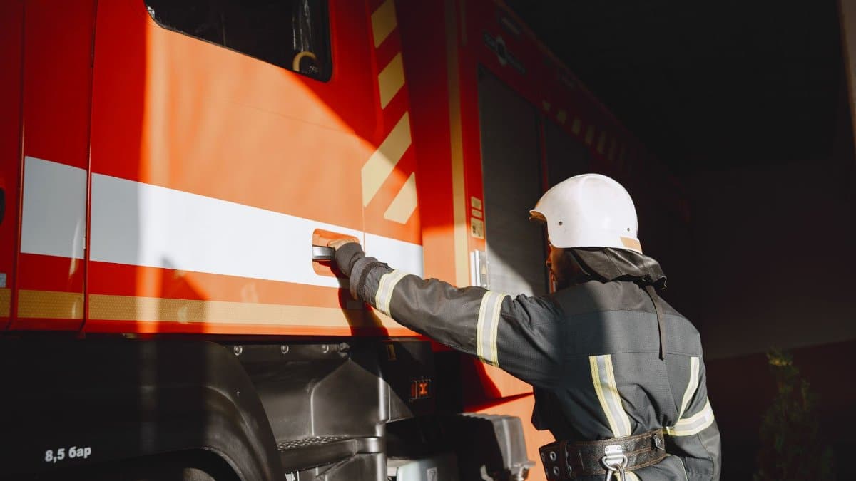 Firefighter in safety gear working with a fire truck outdoors during the day.