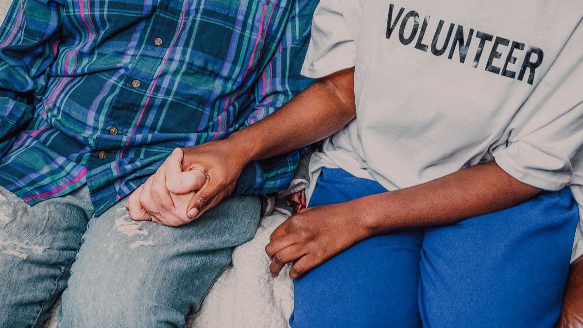 A volunteer holding hands with a senior, symbolizing care and community support.