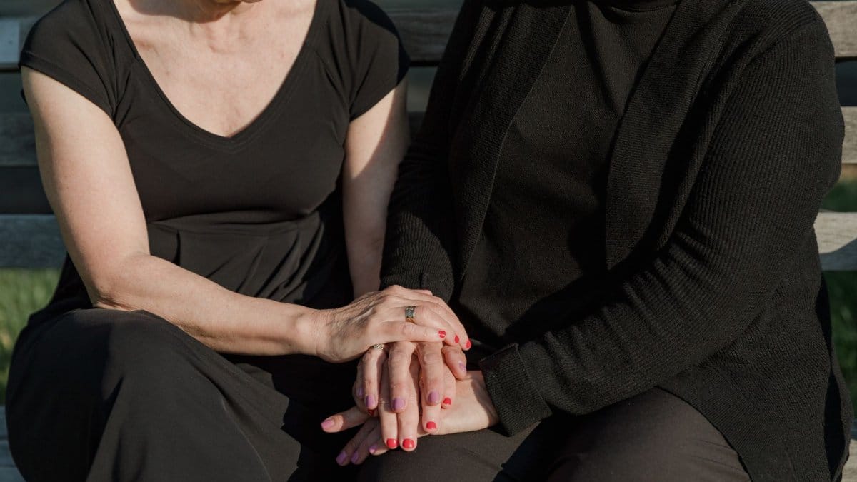 Two women seated on a bench, offering support and comfort to each other.
