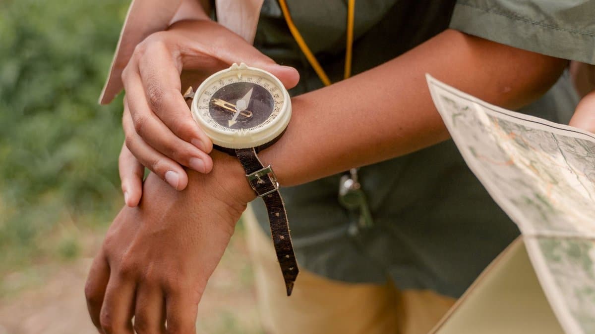 Person using compass and map for navigation outdoors, wearing a scout uniform.