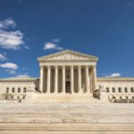 Front view of the United States Supreme Court building on a sunny day with blue sky and clouds.