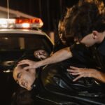 Dramatic nighttime arrest scene with police officers detaining a suspect on a patrol car.