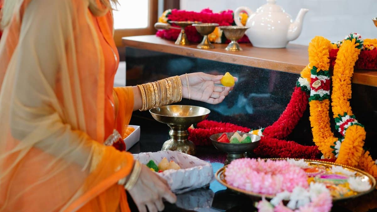 A woman in traditional attire participates in a colorful Indian cultural ceremony with flower garlands and offerings.