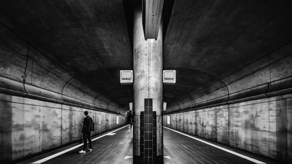 Black and white photo of a person waiting in an underground metro station.