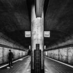 Black and white photo of a person waiting in an underground metro station.