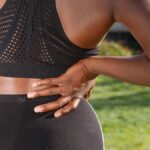 Woman in athletic attire holding her back outside, indicating discomfort or pain.