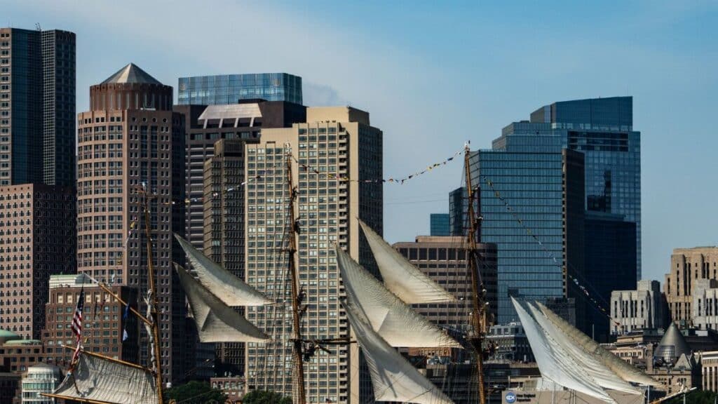 Tall ship with sails unfurled against Boston's modern skyline on a clear day.