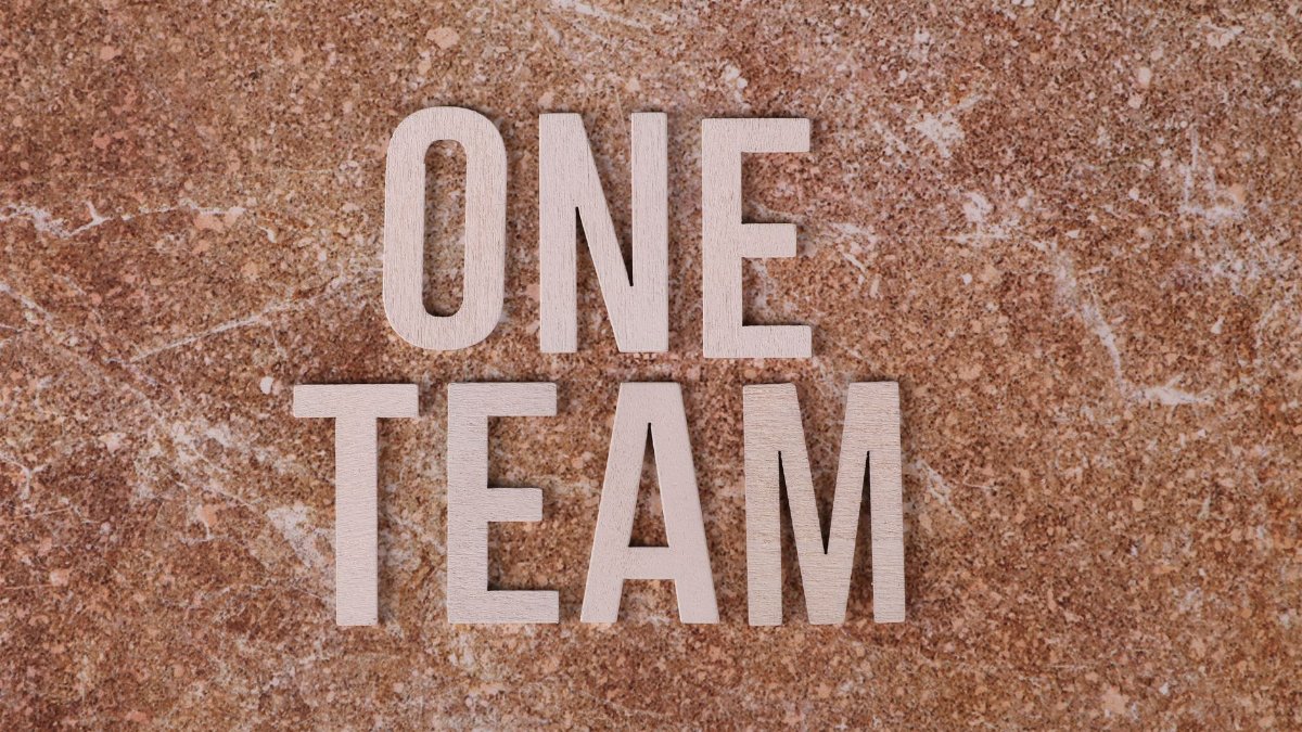 Wooden 'One Team' text on marble background symbolizing unity and teamwork.