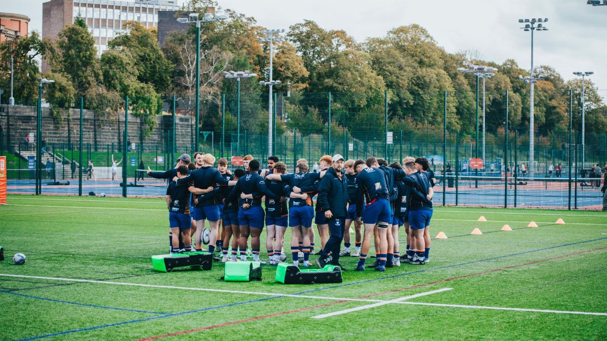 Team of rugby players huddling during outdoor training session on a sports field.