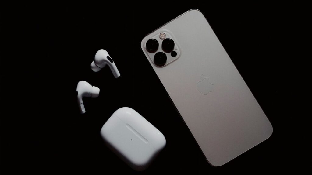 Close-up of smartphone and wireless earbuds on a dark surface, showcasing modern tech gadgets.