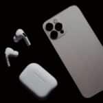 Close-up of smartphone and wireless earbuds on a dark surface, showcasing modern tech gadgets.