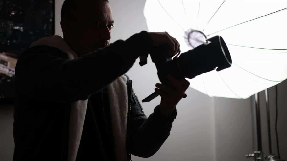 Silhouette of a photographer adjusting a camera during a studio shoot with a large umbrella light.