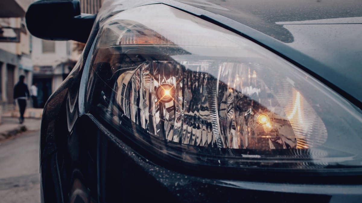 Detailed close-up of a car's headlight on a city street, showcasing urban automotive details.