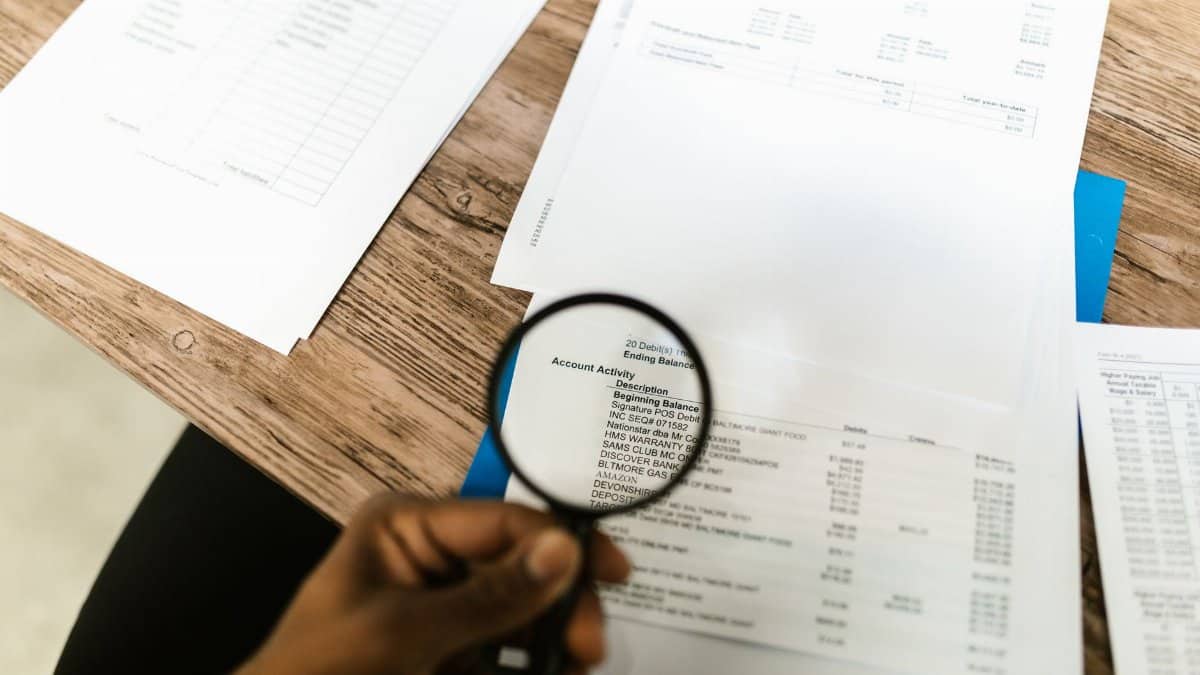 Close-up of hand using magnifying glass to review documents. Ideal for financial themes.