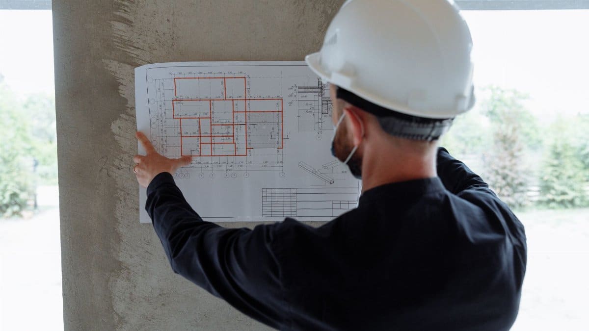 Engineer in hardhat reviewing architectural floor plans at construction site.
