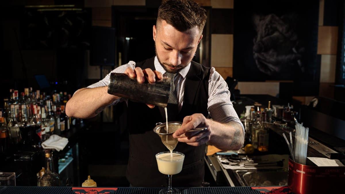 Experienced bartender pouring a cocktail through a strainer, showcasing advanced mixology skills.
