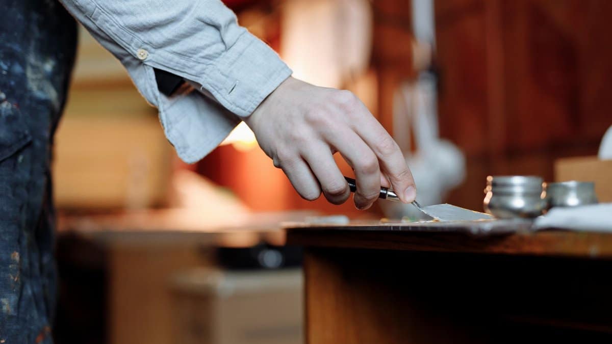 Artist's hand skillfully uses a palette knife indoors for fine art creation.