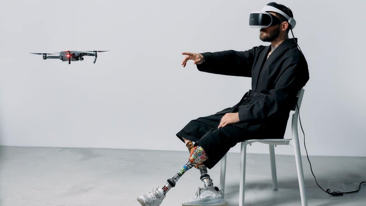 Man with prosthetics using VR headset and drone indoors, embracing technology.
