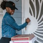 Female delivery driver holding pizza boxes at doorstep ready for delivery.