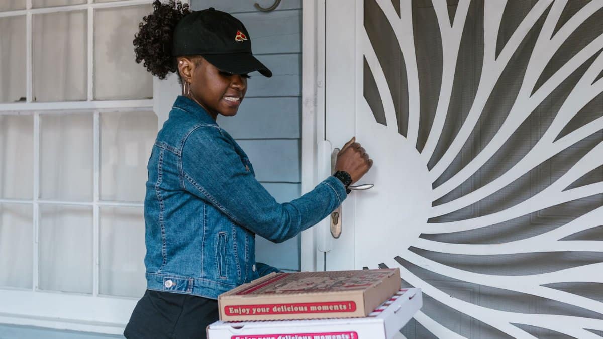 Female delivery driver holding pizza boxes at doorstep ready for delivery.