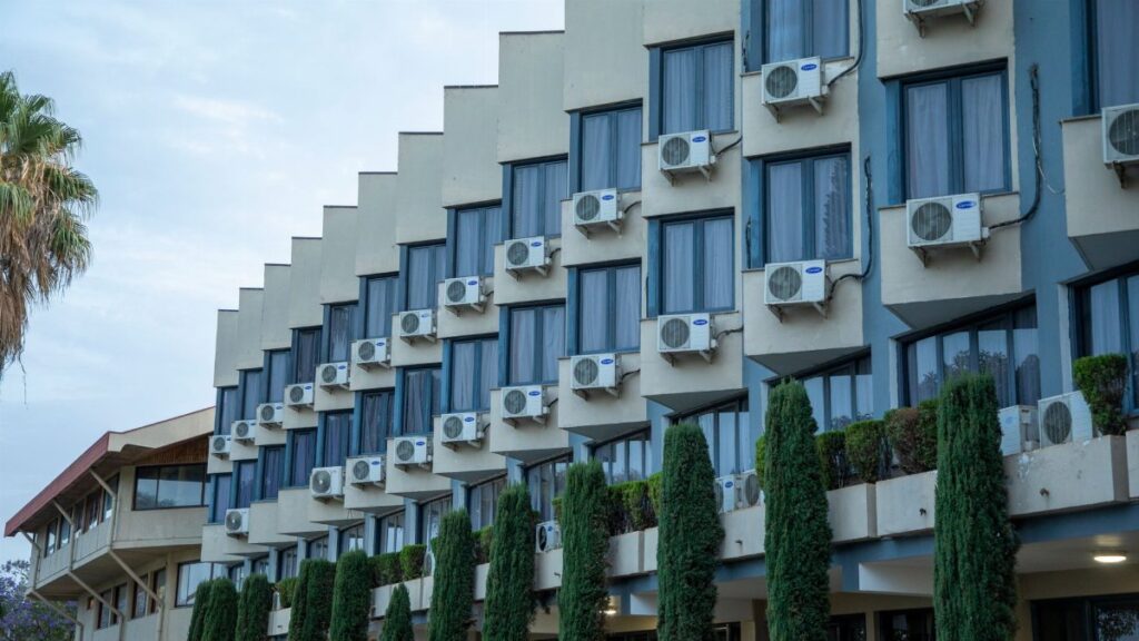 Exterior view of a hotel building featuring rows of windows and air conditioning units, against a clear sky.