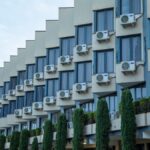 Exterior view of a hotel building featuring rows of windows and air conditioning units, against a clear sky.