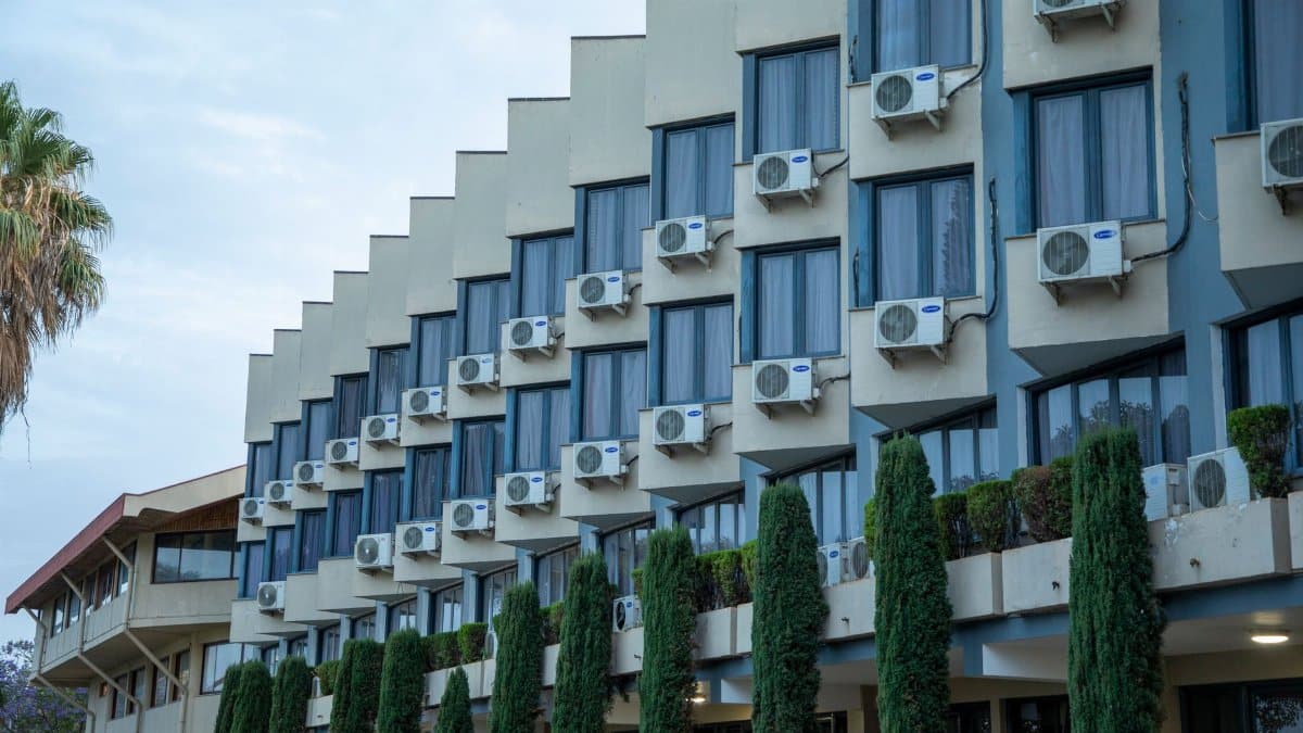 Exterior view of a hotel building featuring rows of windows and air conditioning units, against a clear sky.