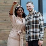 Young couple celebrates buying their first house with keys in hand and a sold sign.