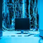 A complex network of cables in a data center with a monitor in the foreground.