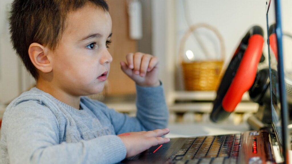 A young child focuses intensely on a laptop screen while learning from home, showcasing modern education.