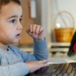 A young child focuses intensely on a laptop screen while learning from home, showcasing modern education.