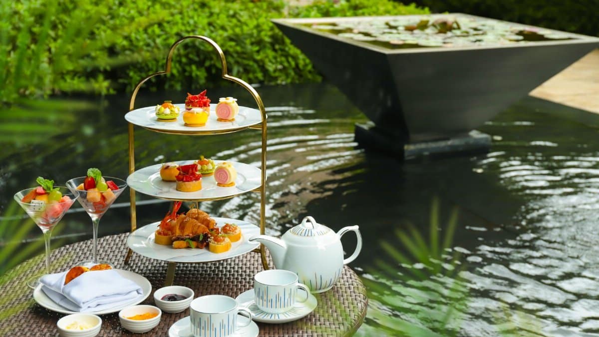 Luxurious afternoon tea setup with pastries and teapot beside a serene garden fountain.