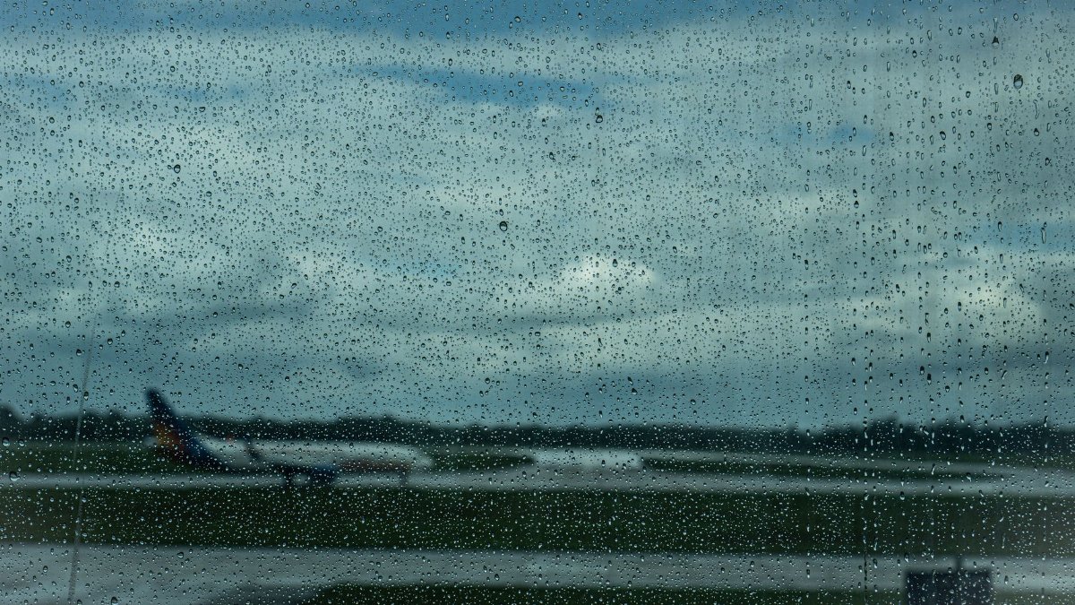 Airplane in the distance through raindrop-covered window at airport.