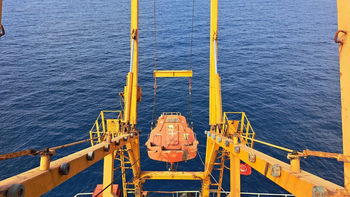 Lifeboat hanging over the ocean from a cargo ship, depicting maritime industry and safety.