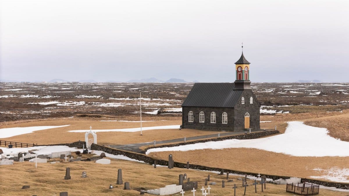 A scenic view of a historical church and graveyard surrounded by Icelandic nature during early spring in Suðurnesjabær, Iceland.