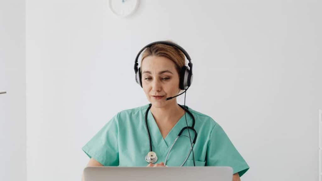 A female doctor in scrubs using a laptop for a virtual consultation, enhancing telemedicine.